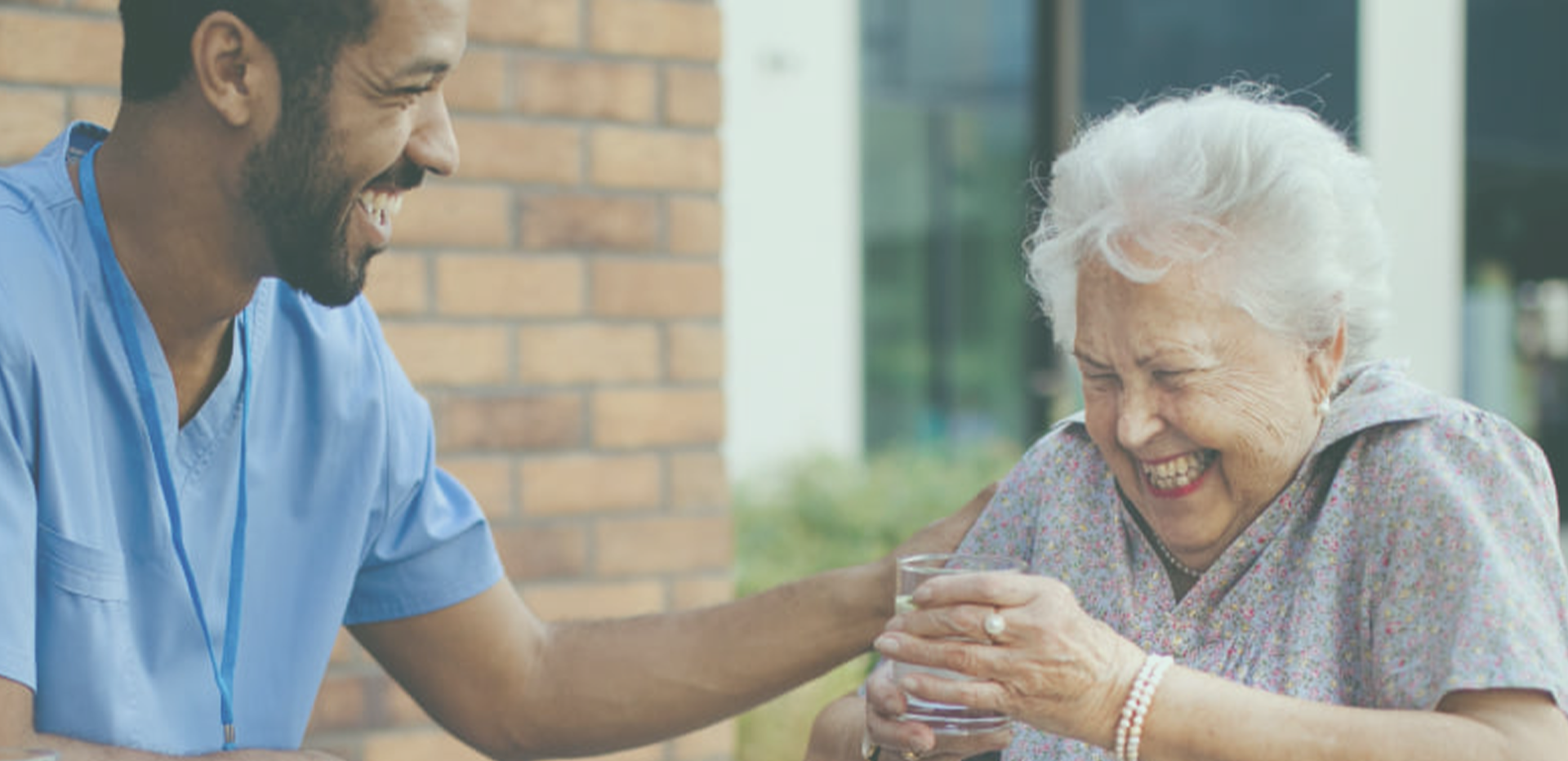 Pflegekräfte und betreute Person lachen gemeinsam in einem hellen Innenraum, freundliche und einladende Stimmung